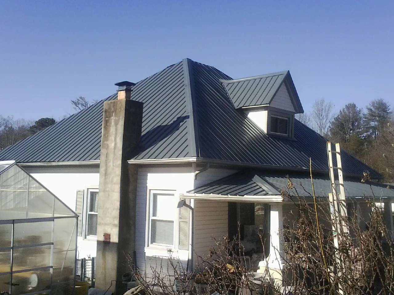Dark blue standing seam metal roof on a white farmhouse with dormer — Slate & Tile Roof Repair by Roofing Brothers in Zearing