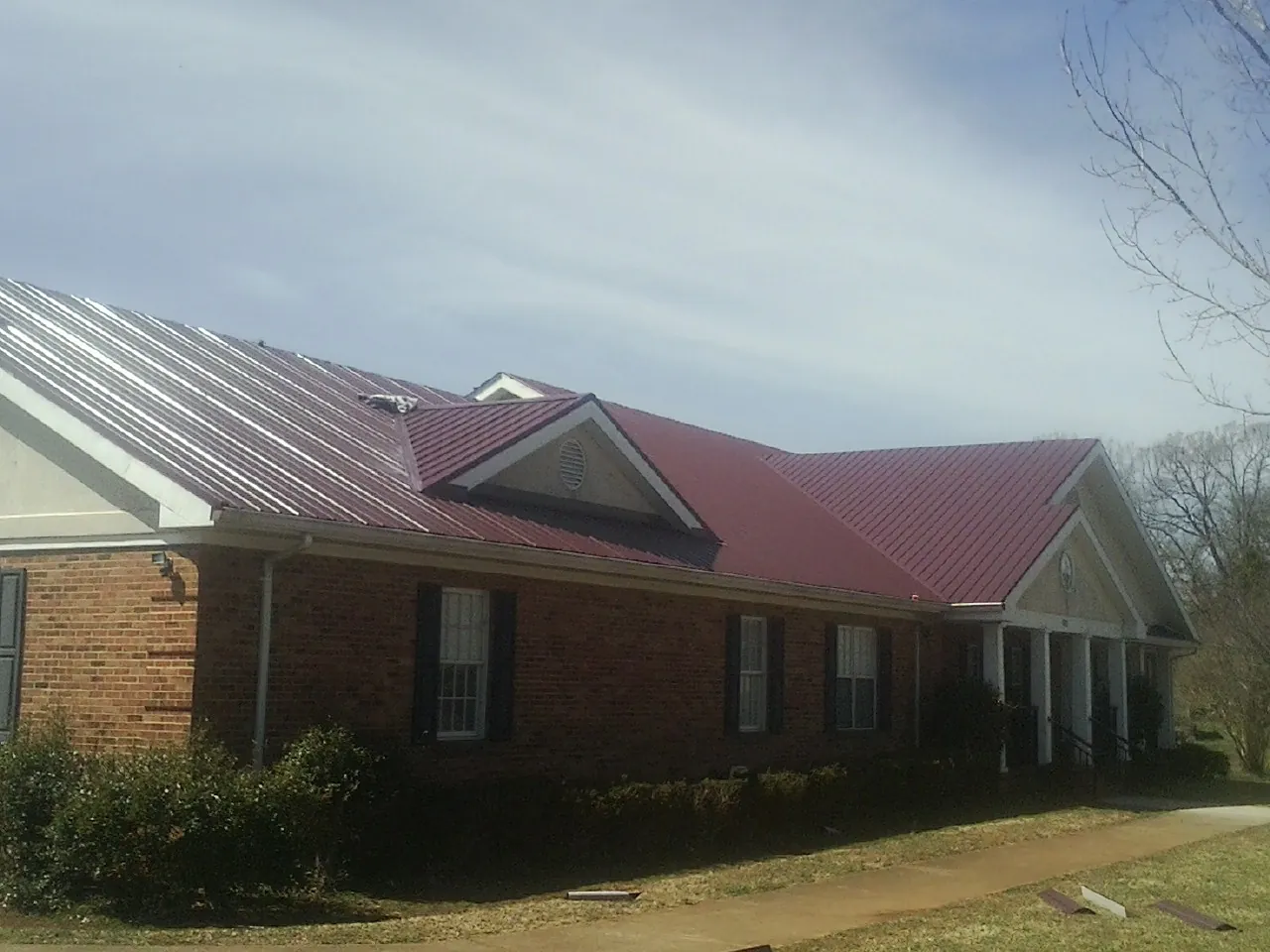 Red metal roof with gabled entries on a long brick building, from a Hail Damage Roof Repair job in Zearing