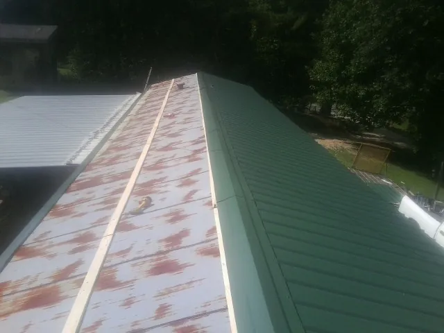 Old rusted panels beside newly installed green metal roofing — Wind Damage Roof Repair by Roofing Brothers in Zearing