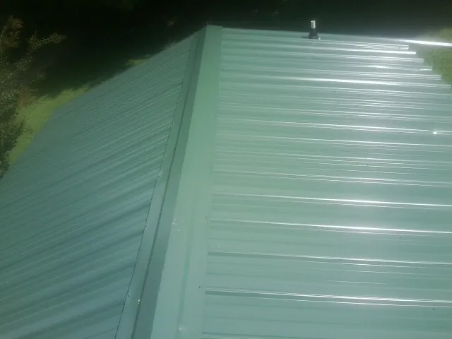 New green metal panels meeting at the ridge of a roof — Flat Roof Repair work by our crew in Zearing