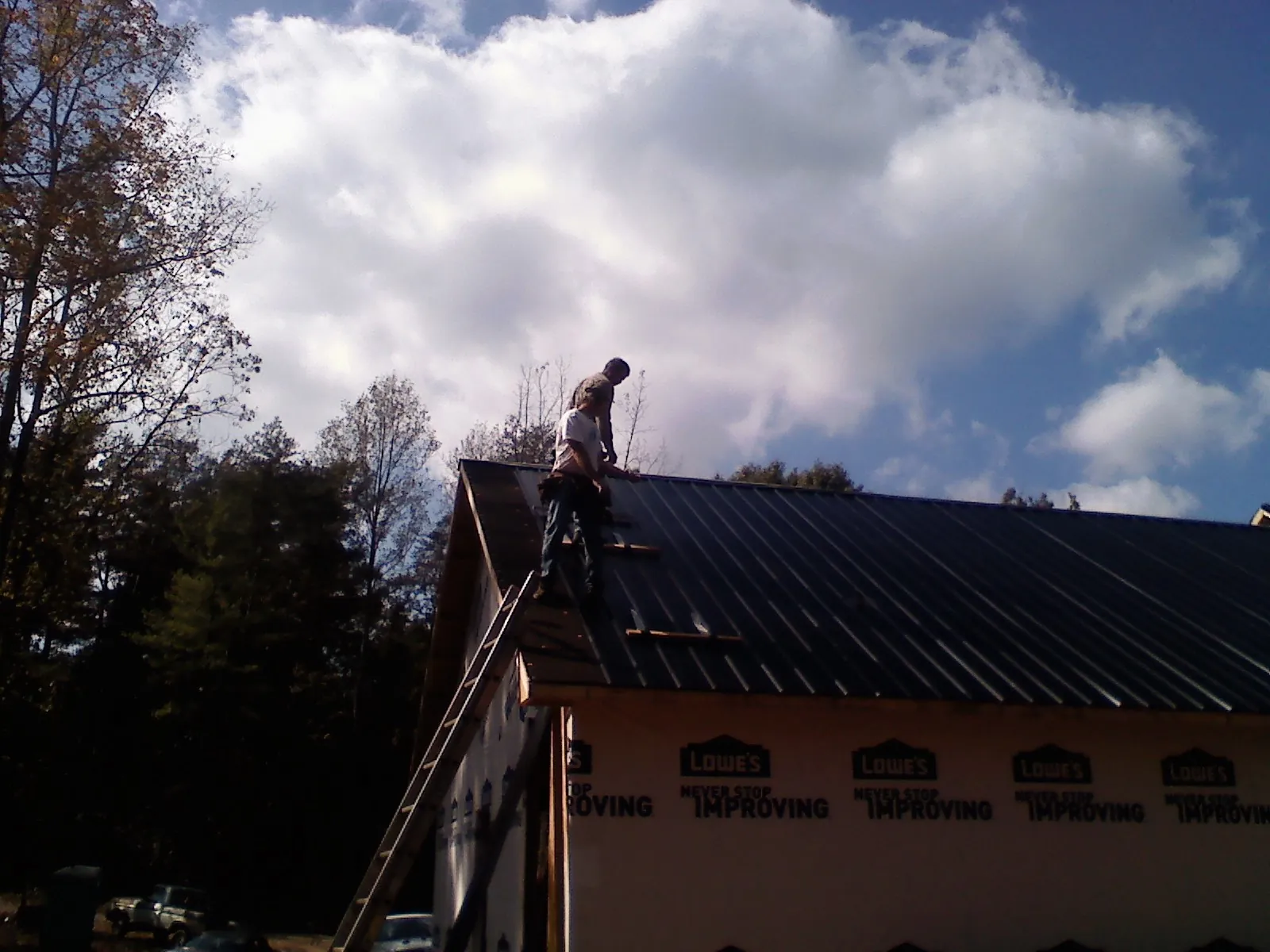 Roofer fastening dark metal panels high against a cloudy sky, from a Roof Inspection job in Zearing