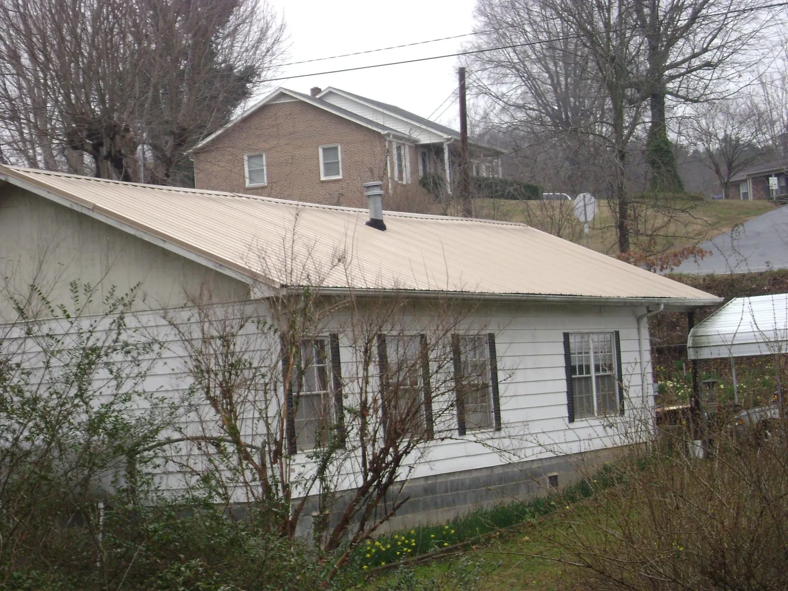 Tan metal roof on a white sided house set into a hillside — Commercial Roofing by Roofing Brothers in Zearing