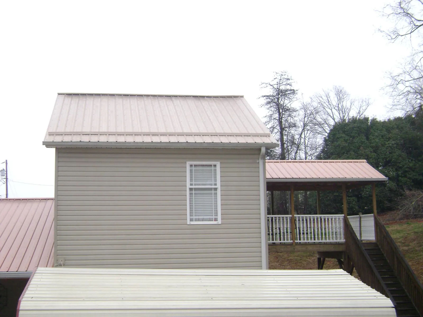 Tan metal roofs on a two story addition and attached porch, from a Roof Replacement job in Zearing