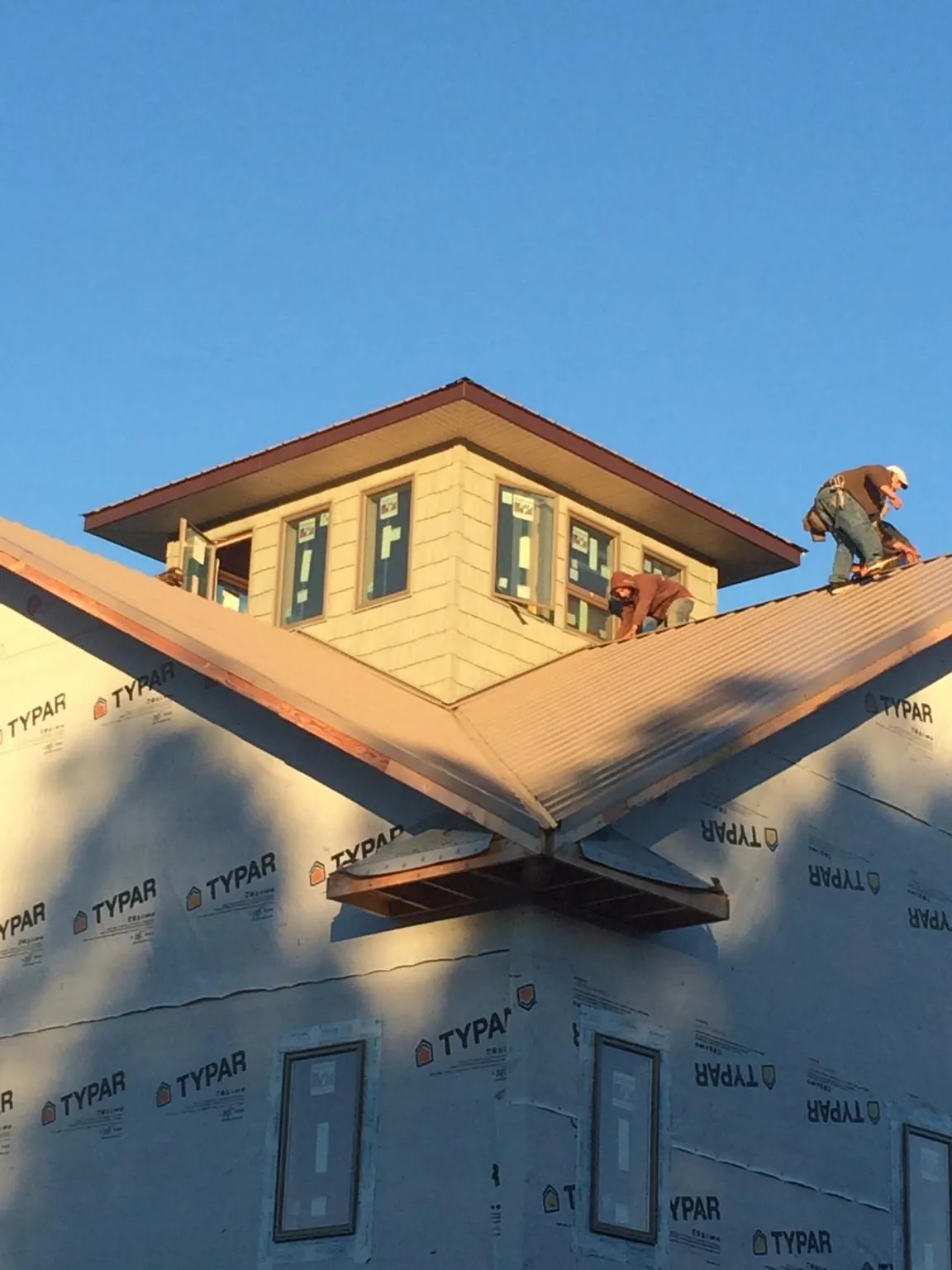Roofers working around a rooftop cupola on a new metal roof at sunset — Roof Waterproofing in Zearing by Roofing Brothers